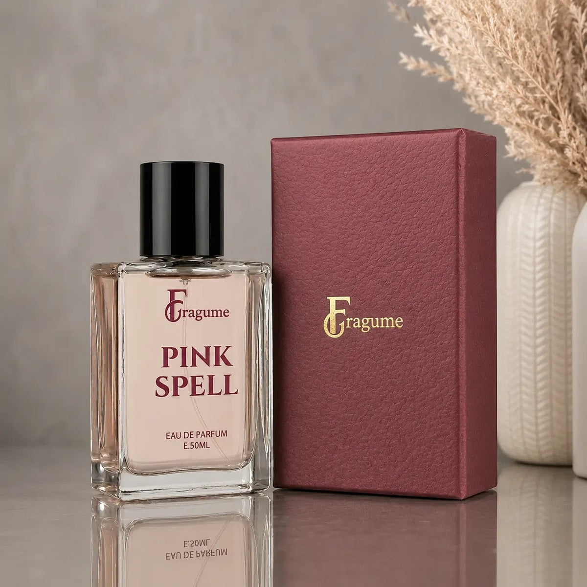 fragume Pink Spell Eau De Parfum in a glass bottle next to a textured maroon presentation box on a grey surface
