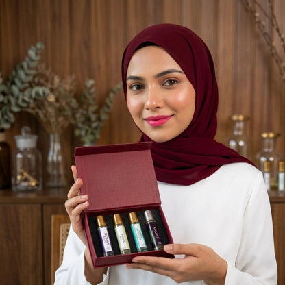A woman in a maroon hijab holding a fragume 4 pocket perfume set with four travel-sized fragrance bottles in a box.