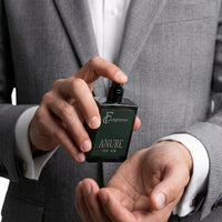 Man in a grey suit spraying Fragume Anure Parfum from a sleek forest green glass bottle onto his wrist.