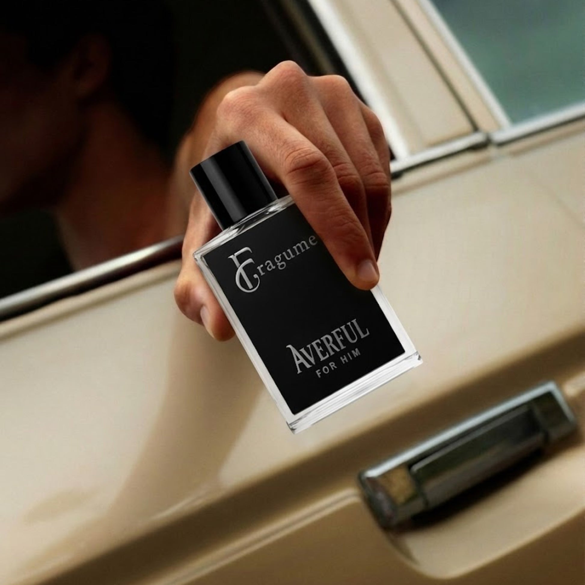 A hand holding a sleek black Fragume Averful Parfum bottle against a luxury car door